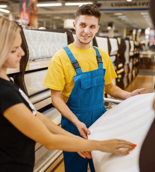 Assistant and female customer choosing wallpapers in hardware store. Seller in uniform and woman in diy shop, shopping in building supermarket