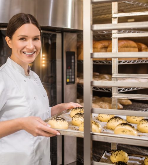 bakery-buns-happy-pretty-woman-in-white-uniform-putting-tray-of-rolls-in-special-rack-to-wait-for-baking-in-oven