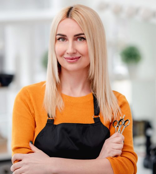 Portret of blond woman hairdresser smiling and holding in her hand scissors