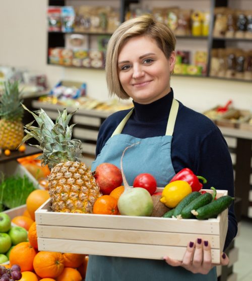 smiling-woman-salesman-holds-wooden-box-with-vegetables-and-fruits-in-the-store