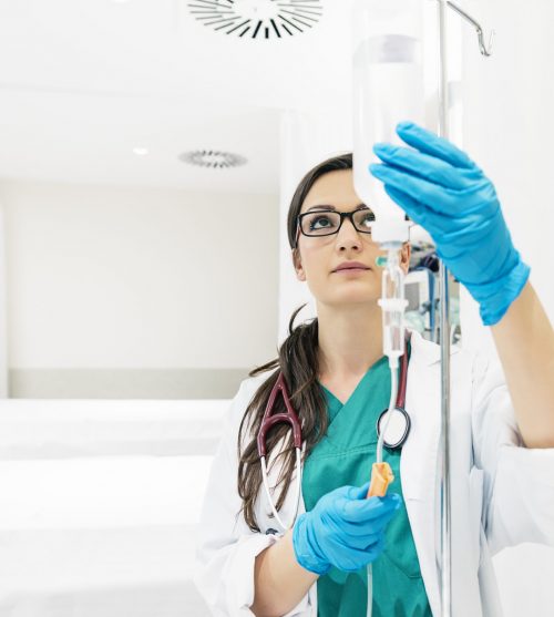 Young woman doctor anesthesiologist dressed in green gown, puts the dropper in hospital room