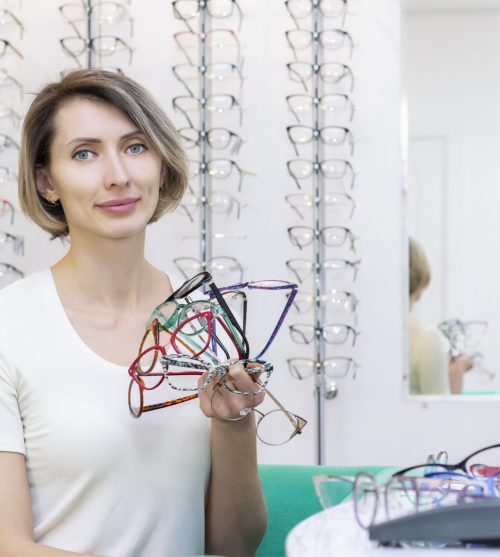 young woman in optic store choosing new glasses with optician. glasses in the store of optics. A woman chooses glasses. many glasses in hand. Ophthalmology.